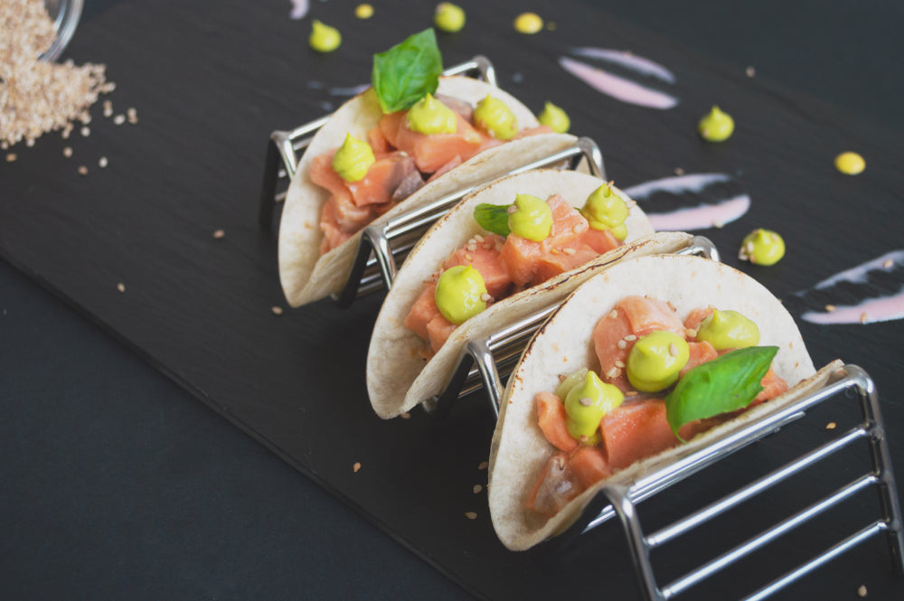 Three salmon and avocado tacos on a metallic taco serving stand