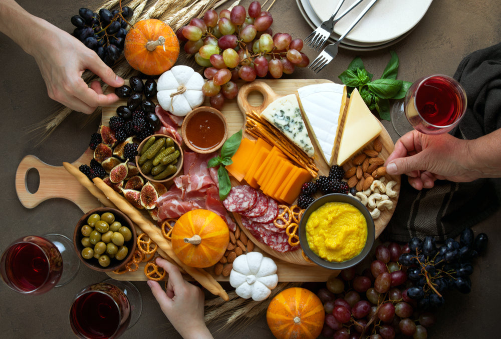 Three people reach for a Charcuterie board filled with different cheese and meats