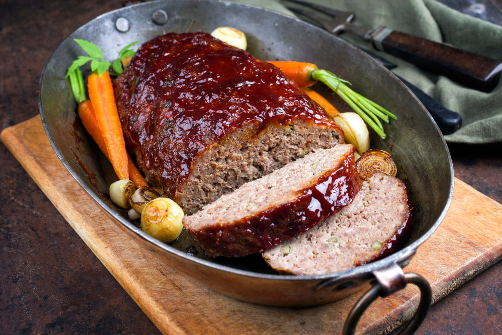 Baking tray with meatloaf surrounded by carrots and other vegetables
