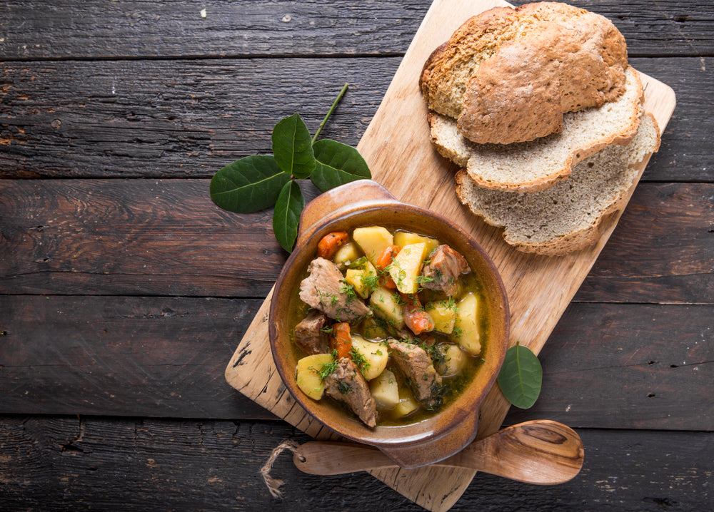 Irish stew in a small bowl next to slices of bread on a wooden cutting board