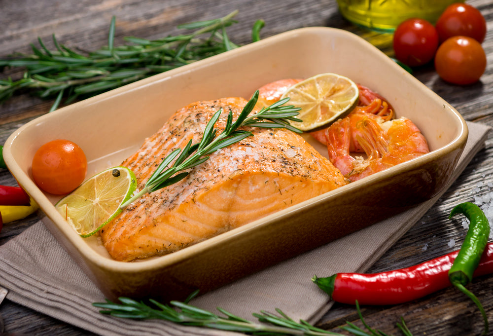 Salmon in a ceramic baking dish with slices of lime and tomatoes as garnish