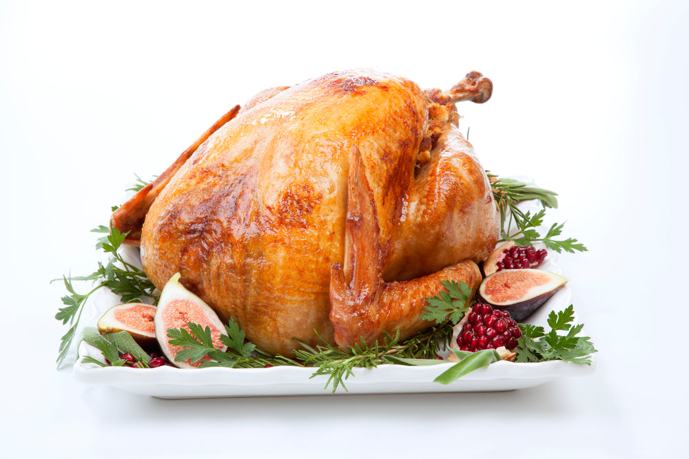 Traditional roasted turkey, garnished with fresh figs, pomegranate, and herbs on white background.