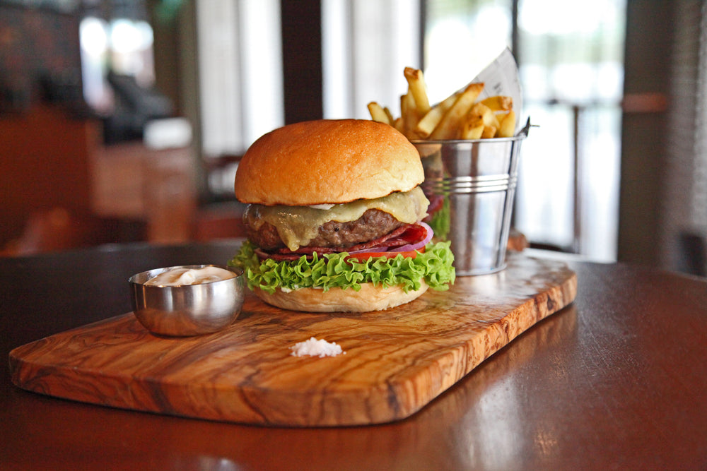 Oven-baked cheeseburger with onion, tomato lettuce and a side of fries on a wooden cutting board