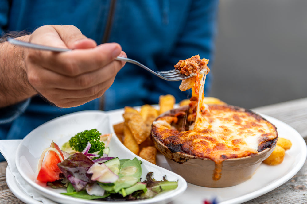 Food on a white plate such as portion of lasagne, chips and salad