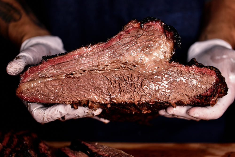 Chef with white gloves holds a sliced piece of smoked beef brisket