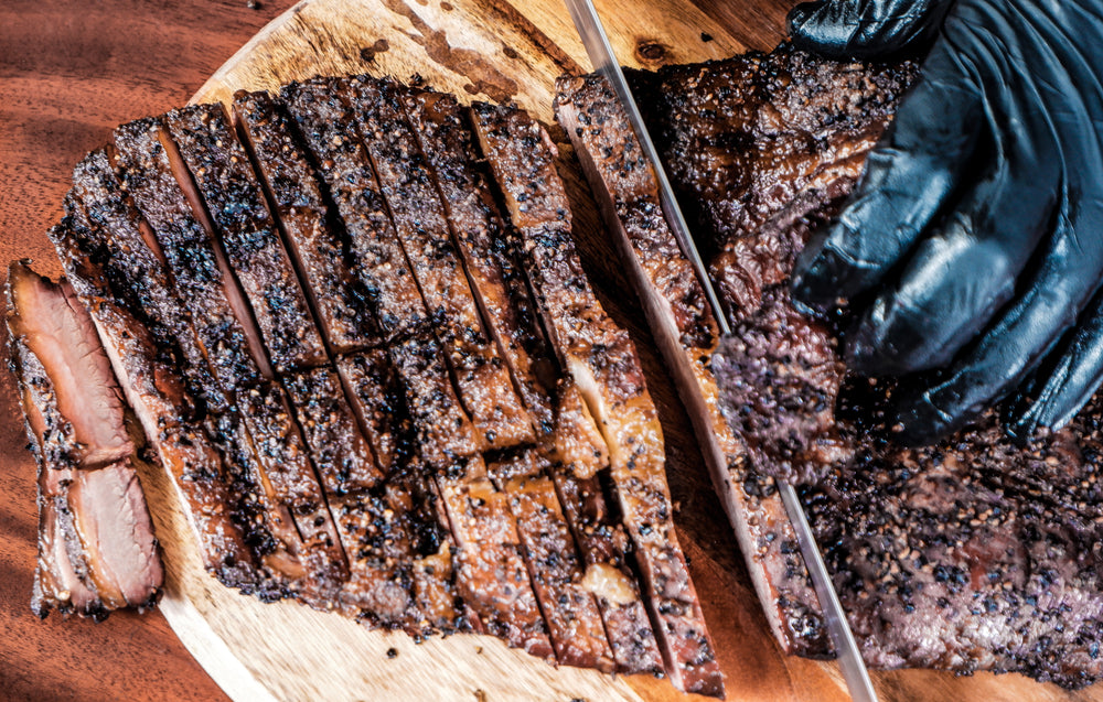 Chef with black gloves slicing through smoked beef brisket