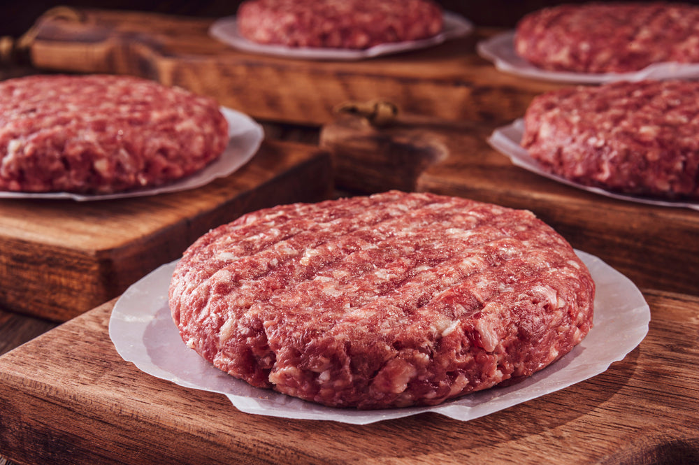 Raw hamburger patties on white parchment paper