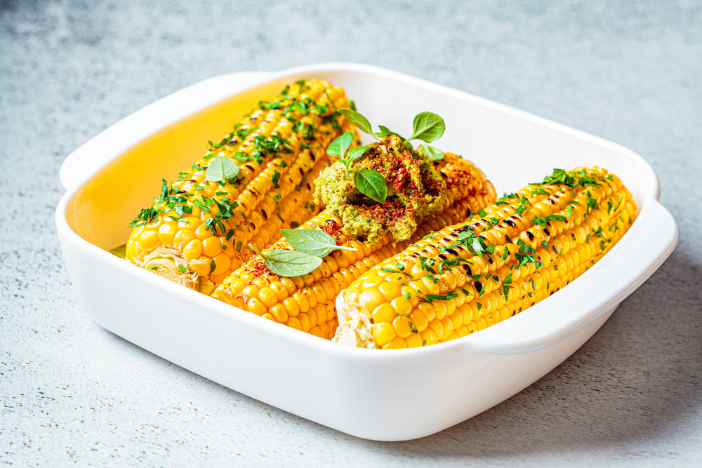 Three pieces of corn on the cob in a white baking dish with green garnish 