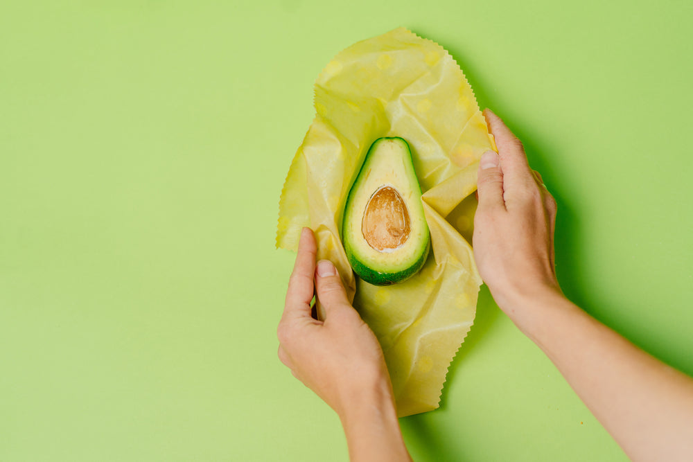 Two hands wrapping half an avocado in parchment paper