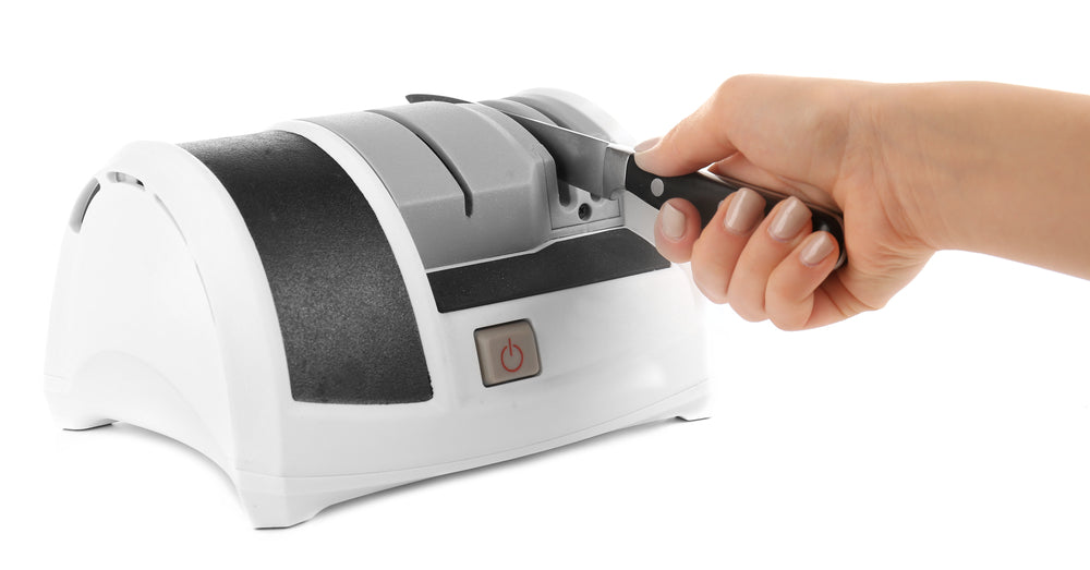 A hand placing a knife through an electric knife sharpener with a white background