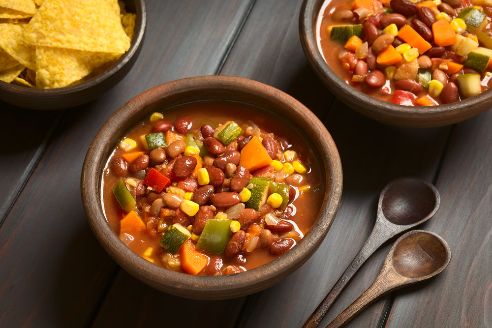 Bowl of vegetarian chili with beans and vegetables next to two dark wooden spoons