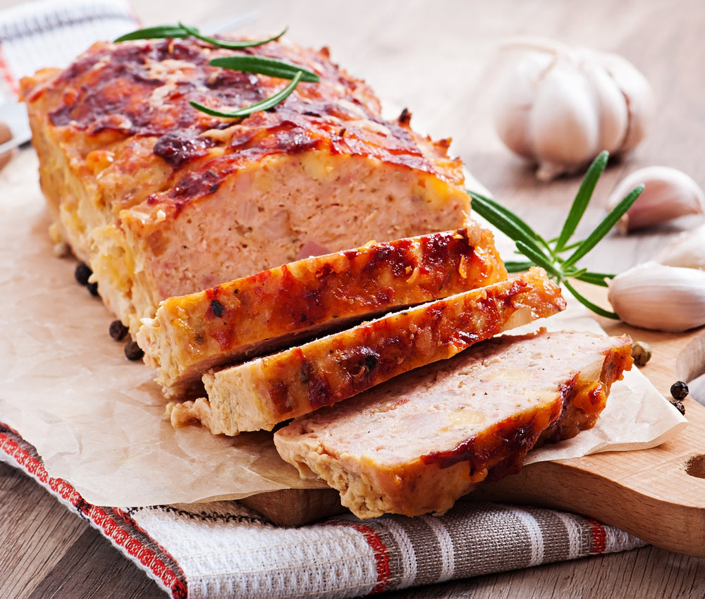 Slice meatloaf on a cutting board that's resting on a kitchen towel with garnish in the background