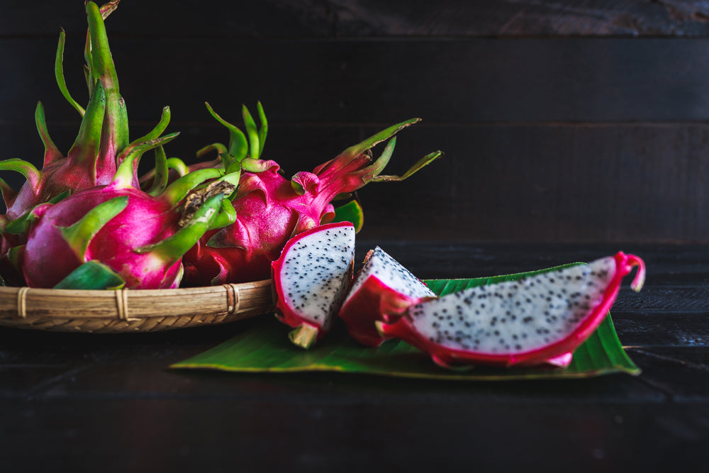 A fruit basket filled with dragon fruit next to a sliced dragon fruit 