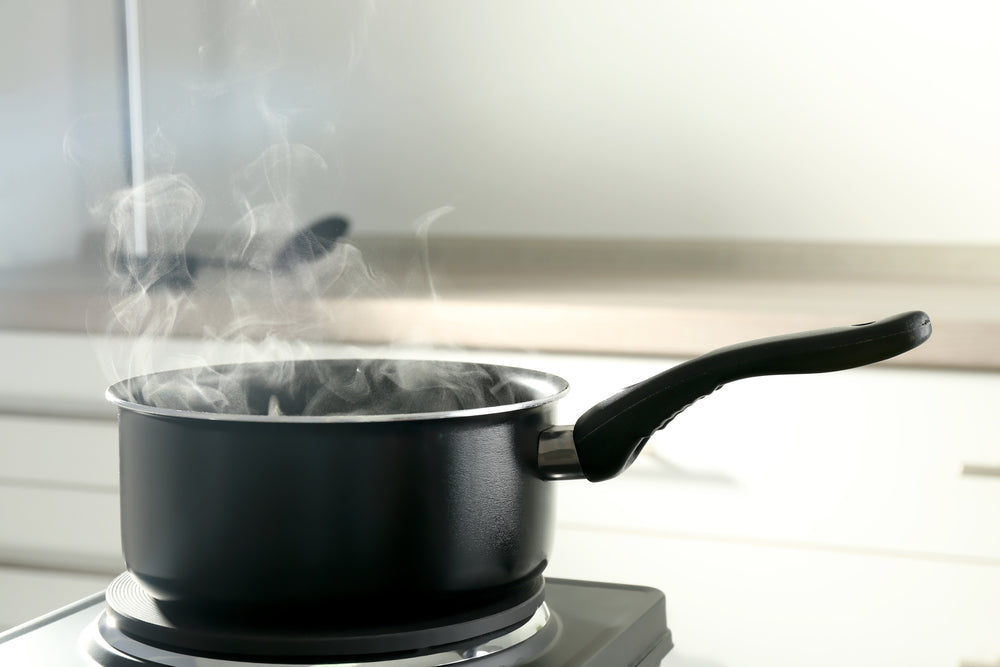 A black metalic saucepan on a kitchen stove with steam rising 