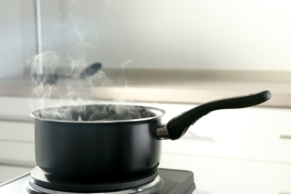 A black metalic saucepan on a kitchen stove with steam rising