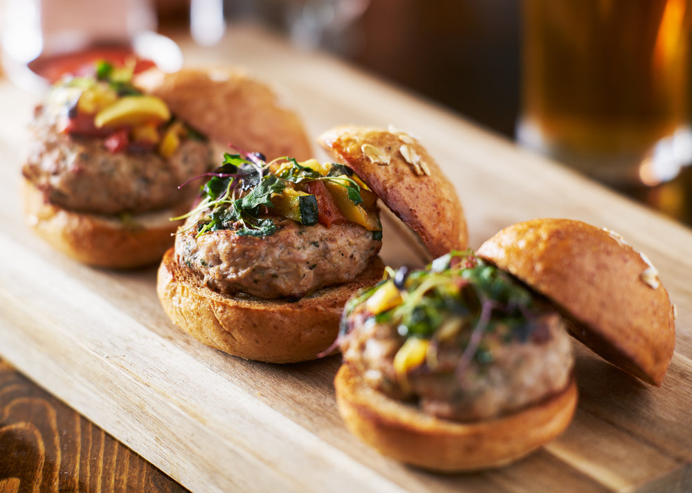 Three turkey slider oven baked burgers topped with garnish on a wooden table