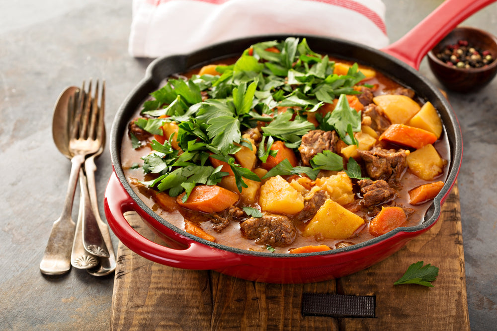 Traditional Irish Stew in a red skillet on a wooden cutting board next to a fork and spoon