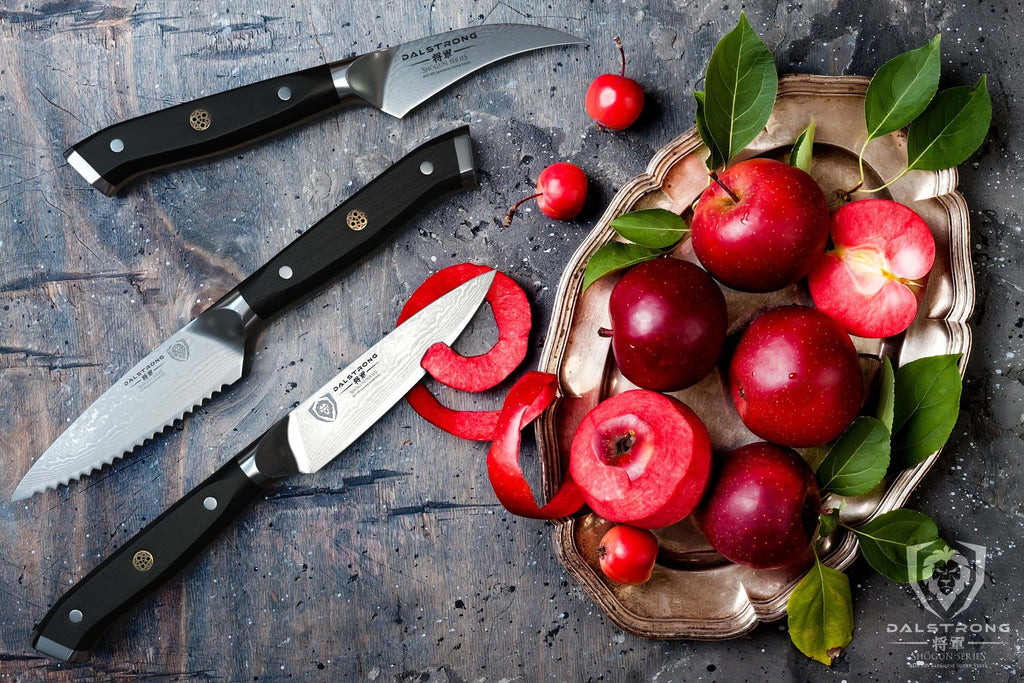 Three sharp paring knives against a grey background next to red fruit