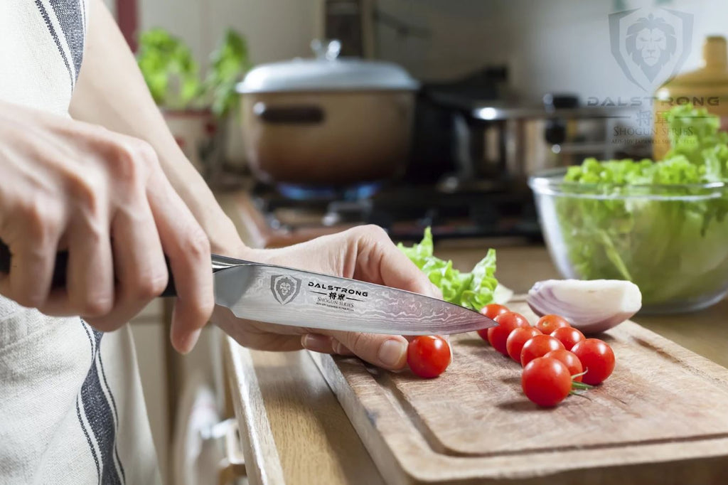 Shogun Paring Knife cutting cherry tomatoes on a wooden cutting board with lettuce and other ingredients on the side.