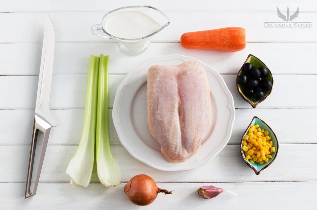 Dalstrong Crusader Boning Knife on a white wooden table surrounded by chicken breast and other ingredients.