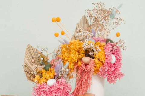 Image or brightly coloured floral arrangements featuring dried pink hydrangea, billy buttons, fan palms and bunny tails