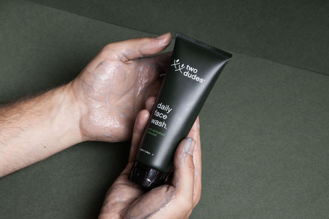 two white skin toned hands with soap bubbles on them, cradling a tube of mens face wash