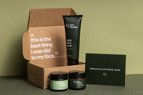 packaging with skincare tubes and tubs by Two Dudes brand, with a note saying 'welcome to the family, dude' and a goof testimonial saying "this is the best thing I ever did to my face' - you, after using Two Dudes"