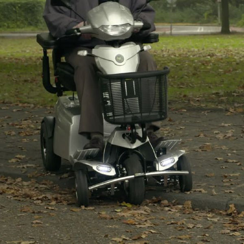 A heavy-duty mobility scooter, the Quingo Toura 2, is shown in this image. The scooter is designed to easily climb curbs, as depicted in the picture.