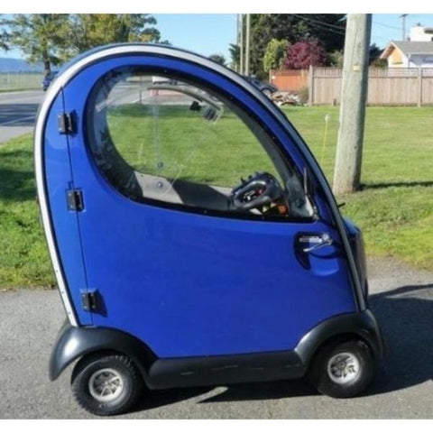 Image of a blue enclosed scooter, the Shoprider Flagship. The scooter is parked outdoors and is designed for comfortable and safe mobility.