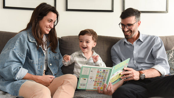 A Mom and a Dad are laughing while reading a book to their son. Musical books, kids, language, skills.