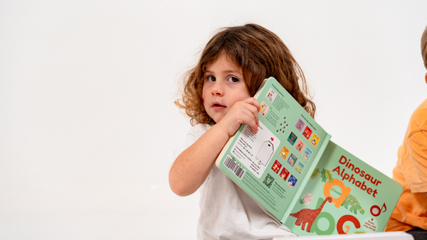 A toddler girl is holding a dinosaur book. Dinosaurs, fun activities, education, children books.