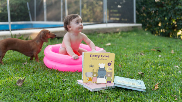 In the background a dog and a baby is playing in a small inflatable pool and at the front is a musical picture book for kids. Children books, fun activities, educational.