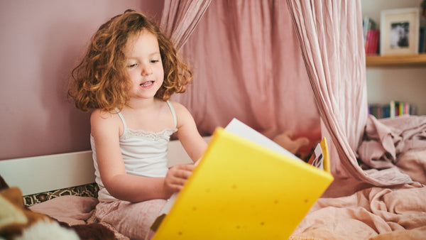 A toddler girl is reading a book in bed. Bedtime stories, kids activities, educational.