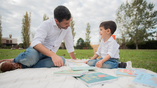 A dad is reading books in the garden with his young boy. Screentime, kids activities, fun, educational.