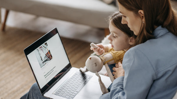 A Mom is looking at her laptop with her young daughter. Family, travel tips.