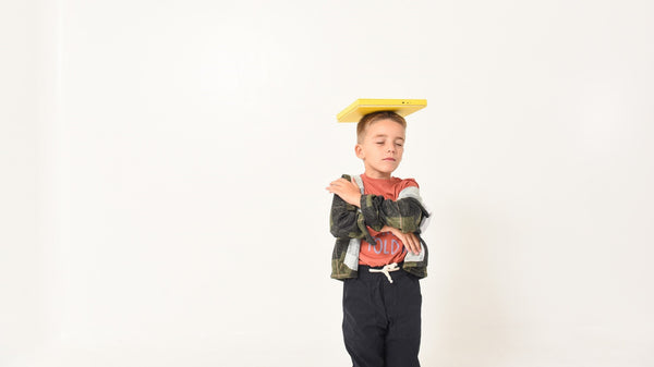 A young boy is closing his eyes and balancing a book on his head. Self regulation, tantrums, breathwork, kids emotions.