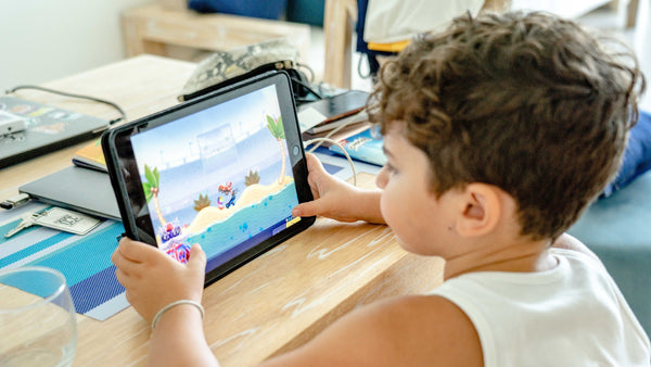 A small boy is sitting at a desk and playing on an ipad. screentime, kids activities, fun, educational.