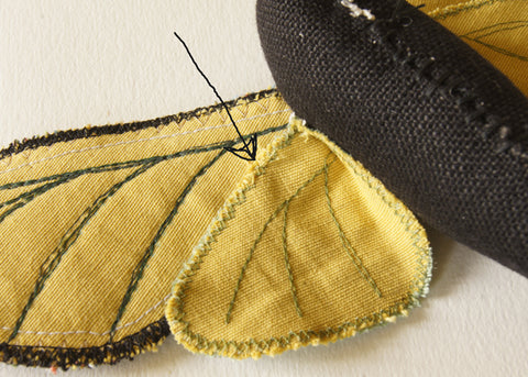 underside of wings, with arrow pointing to whipstitches which join the lower wing to the upper wing