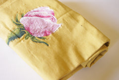 a rolled piece of yellow canvas upholstry fabric (cotton) with a machine embroidered rose in the center.