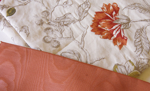 cream upholstery brocade with orange flowers next to a small piece of orange satin