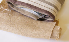 a rolled up piece of natural colored burlap, next to a folded piece of beige and brown striped canvas fabric. 