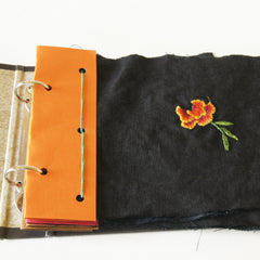 two ring binder open to show orange header sewn to marigold embroidery sampler