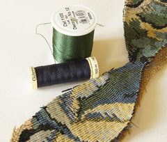green thread and dark blue thread placed next to tapestry fabric for choice