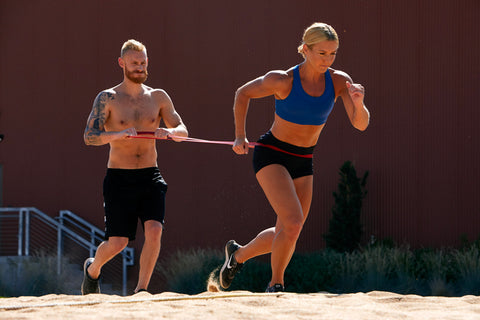 Man & woman work out with a large resistance band in sand pit