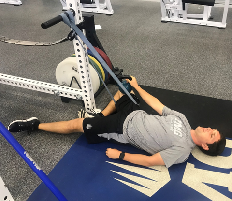 Man does a hip-opening stretch at the gym with a SPRI Superband and Kettlebell