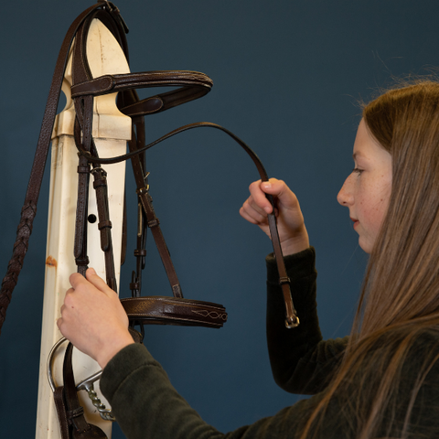 Girl cleaning equestrian bridle