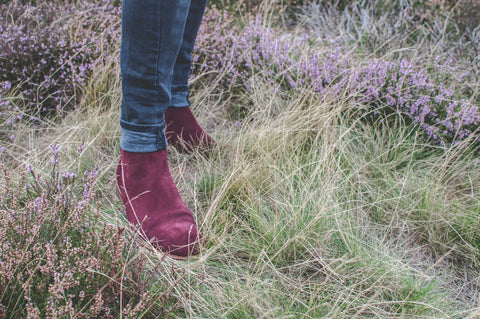 A man's legs in a field of purple flowering heather, wearing Hamilton suede chelsea boots in bordo. 