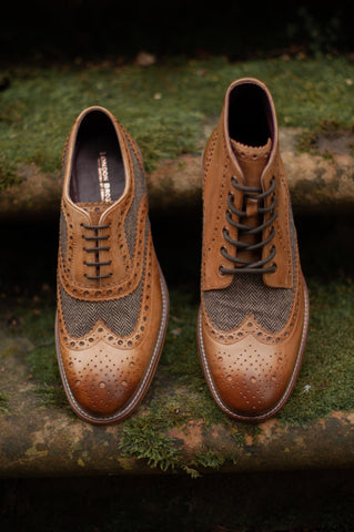 A tan and tweed Gatsby shoe sits on a moss covered step next to a tweed and tan Gatsby boot 