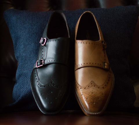 Two leather Leonard monk strap shoes, one black on tan are propped up on a velvet cushion