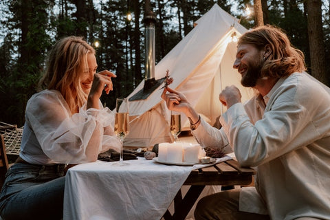 couple glamping in woods and eating a candle lit meal together